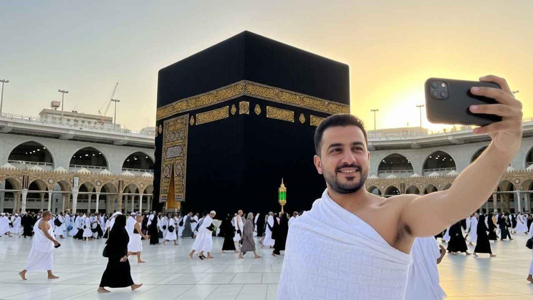 man take a selfi photo performing umrah wearing ihram with background of kaaba